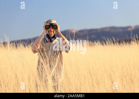 Safari homme regardant à travers les jumelles dans l'herbe haute Banque D'Images