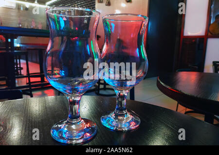 Verres pour les cocktails de près. Sur une table de bois dans le bar sont deux verres vides en verre avec des reflets bleus. Plats pour des boissons alcoolisées. Banque D'Images