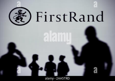 La FirstRand Bank logo est visible sur un écran LED à l'arrière-plan tandis qu'une silhouette personne utilise un smartphone (usage éditorial uniquement) Banque D'Images