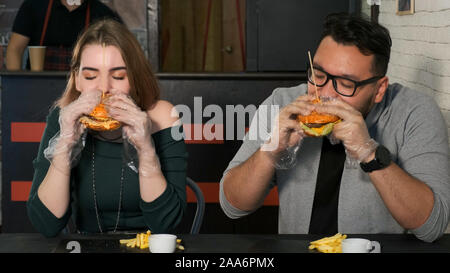 Eating burgers couple multiracial dans un café. Asian guy mord un délicieux burger Banque D'Images