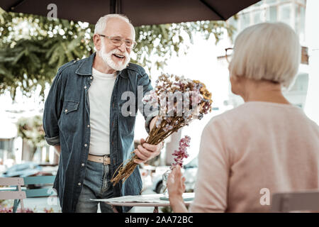 L'homme heureux joyeux donnant des fleurs à une femme âgée. Banque D'Images