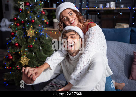 Smiling copain et copine à santa hats tenant la main à Noël Banque D'Images