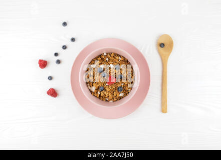 Plaque rose avec granola et fruits rouges sur fond de bois blanc. Vue d'en haut. Concept de vie et d'aliments sains. Banque D'Images