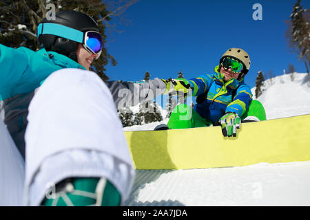 Femme masquée faisant la liaison avec happy man with snowboard assis sur le flanc de la journée d'hiver Banque D'Images