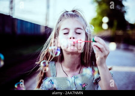 Portrait d'une belle petite fille soufflant des bulles de savon. Un enfant joue avec des bulles, sur un fond vert. Piscine Banque D'Images