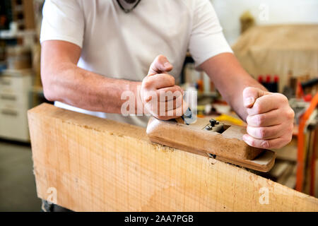 Carpenter raboteuse la surface d'un panneau de bois avec un plan de manuel dans une vue en gros plan sur ses mains et l'outil Banque D'Images