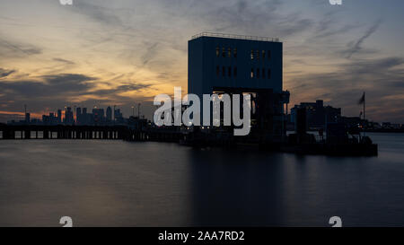 Londres, Angleterre, Royaume-Uni - 21 septembre 2019 : Le soleil se couche derrière la Woolwich Ferry Pier, avec l'horizon de les Docklands de Londres dans la distance. Banque D'Images