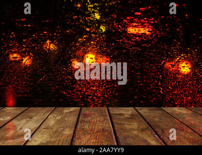 Gouttes de pluie sur la surface du verre avec bokeh rouge les lumières de la ville de nuit avec table en bois Banque D'Images