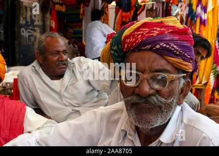 Bikaner, Rajasthan, Inde : portrait d'un homme indien âgé avec turban et lunettes, assis en face d'un magasin de tissu. Banque D'Images