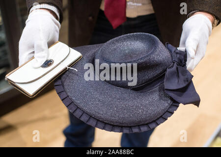 Grasbrunn, Allemagne. 20 Nov, 2019. Un employé de la maison d'enchères détient un portefeuille en cuir peint partiellement (l) et un chapeau de paille noir et bleu par Eva Braun dans ses mains à la maison de vente aux enchères 'Hermann Historica'. Dans la maison de vente aux enchères à Munich, de nombreux objets de dévotion nazis sont mis aux enchères lors de cette journée. Lors de la vente aux enchères un total de 842 articles seront vendus aux enchères, y compris de nombreux effets personnels des anciens grands de Nazi. Credit : Matthias Balk/dpa/Alamy Live News Banque D'Images