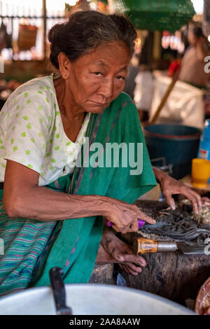 Le quartier animé de viande, poisson, légumes et fruits du marché Pakokku, Myanmar (Birmanie) avec une femme plus âgée la préparation/vendre des fruits de mer avec un froncement de sourcil Banque D'Images