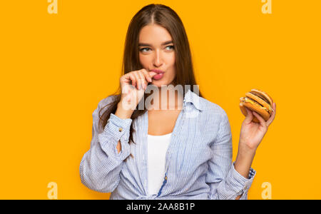 Hungry Girl Holding Burger debout sur fond jaune Banque D'Images