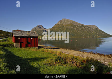 Hangar à bois rouge Lia avec l'île de Aldra et le Hjarttinden peaks derrière, au nord-ouest de la Norvège. Banque D'Images