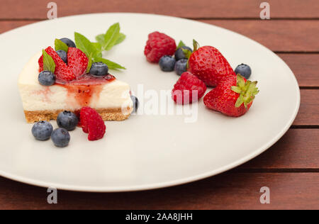 Close up de gâteau au fromage aux fraises, bleuets, framboises et coulis de fruits et crème de menthe sur fond de bois avec plaque Banque D'Images