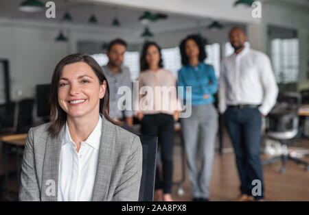 Businesswoman smiling avec des collègues debout dans l'arrière-plan Banque D'Images