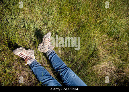 Jambes en jeans et des bottes de randonnée portant dans les hautes herbe verte Banque D'Images