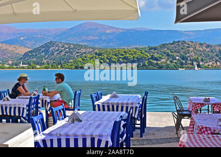 Jeune couple en prenant un verre dans un café avec vue sur l'entrée d'eau d''Argostoli, au village de Drapano. Chaîne de montagnes spectaculaires derrière. Banque D'Images