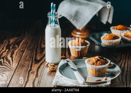 Caramel vanille muffins dans des gobelets en papier et des bouteilles de lait sur fond de bois sombre. Délicieux petit gâteau aux raisins secs, amandes et noix. Des biscui Banque D'Images