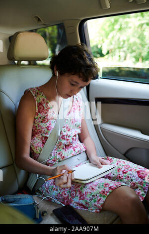 Adorable créatrice preteen girl attaché dans siège arrière de voiture et dessin lors de voyage Banque D'Images