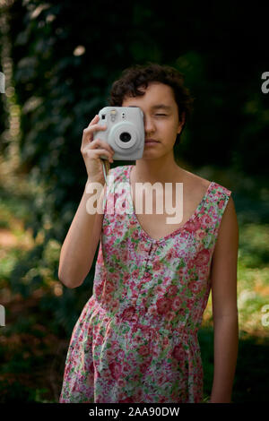 Adorable preteen girl holding photo appareil photo instantané et fermer les yeux en green park Banque D'Images