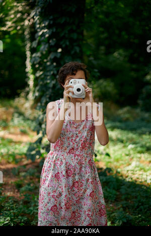 Adorable preteen girl holding photo appareil photo instantané et fermer les yeux en green park Banque D'Images