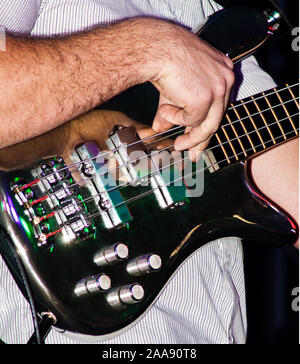 Gros plan sur un guitariste de basse pour le groupe 'Backstreet Soundsystem' pelle les cordes avec dextérité. Sur fond noir Banque D'Images