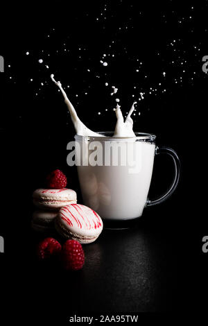 Verre de lait et lait splash sur fond noir avec décoration kiss meringue Banque D'Images