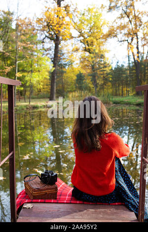 Une jeune femme assise avec son dos sur un pont près d'un lac sur une journée ensoleillée. Belle automne Banque D'Images