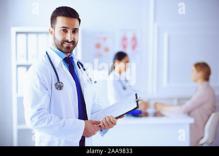 Smiling arabe le médecin de l'hôpital de tablettes et stéthoscope, travailler avec l'équipe médicale du patient sur l'arrière-plan Banque D'Images