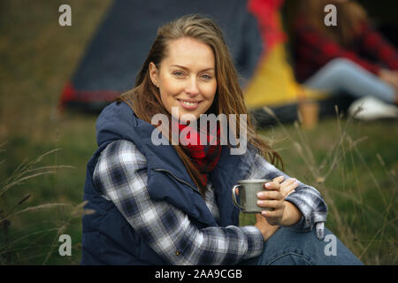 Close up of woman smiling et boire le thé avec un groupe d'amis, sur un arrière-plan sur le camping en forêt. Avoir briser dans la forêt, parlant, laughting. Activité de loisirs, l'amitié, de semaine. Banque D'Images