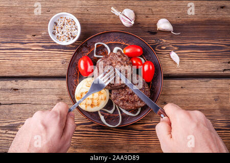 Burger cuit la viande sur fond de bois avec mens mains avec fourchette et couteau Banque D'Images