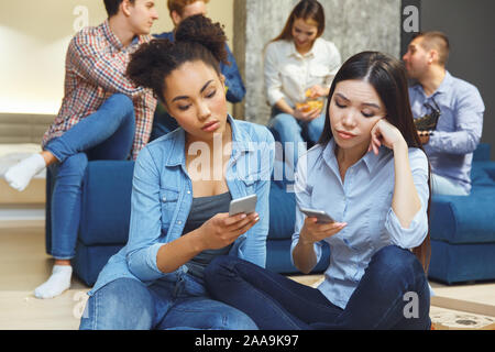 Groupe d'amis ayant des parties à l'intérieur du plaisir ensemble deux filles sitting bored Banque D'Images