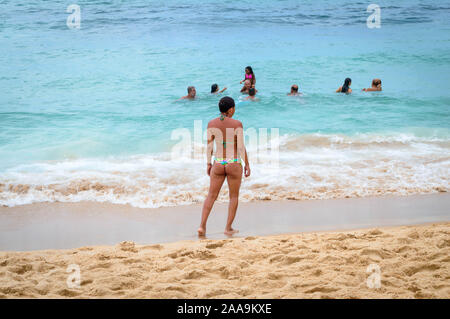 Une femme portant un petit bikini se distingue par l'eau à regarder les gens qui sont la baignade dans l'océan. Banque D'Images