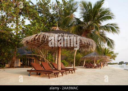 Plage transats sous les parasols de paille. Littoral de l'océan Indien sur l'île des Maldives. Plage de sable blanc et une mer calme. Voyages et vacances. Banque D'Images