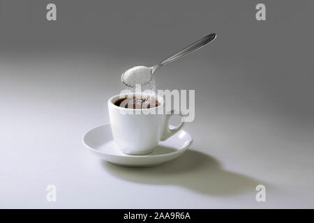 Photo de tasse de café im le milieu de fond neutre avec cuillère flottant dans l'air de verser le sucre dans l'espace de copie. Banque D'Images