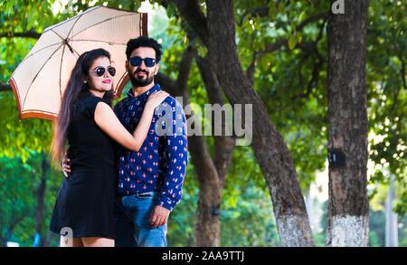 Jeune couple indien en parc avec parapluie portant robe de l'ouest et de l'ombre Banque D'Images