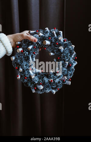 La main de femme dans un chandail blanc de l'hiver de couronnes de Noël est titulaire d'un sur fond sombre. Banque D'Images