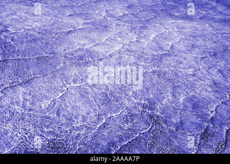 Résumé fond vide naturellement créés par de petites vagues en eaux peu profondes et de la lumière du soleil les réflexions sur la surface de l'eau. Dans les tons de violet un mélange Banque D'Images