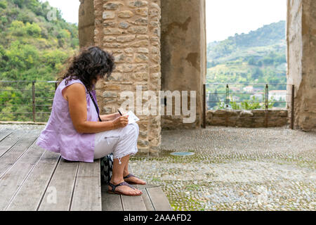 Une femme écrit voyageur cartes postales comme elle s'assoit à l'intérieur de l'ancien château dans le village de Dolceacqua, Italie. Banque D'Images