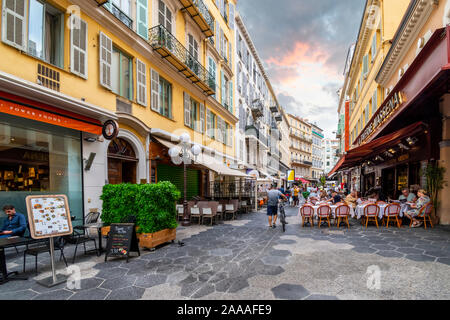 Un homme marche sa bicyclette passé des terrasses de cafés au crépuscule dans le centre touristique de Nice, France, sur la côte d'Azur. Banque D'Images