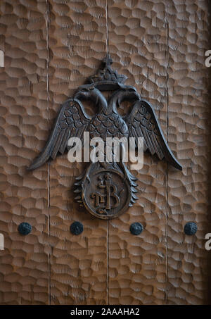 Un aigle aux ailes déployées portant une couronne d'une croix sur une porte en bois martelé. Banque D'Images