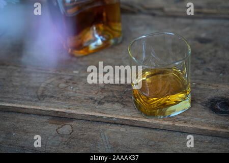 Verre et bouteille de whisky brillant doré sur un vieux tonneau en bois miteux, élément flou en premier plan Banque D'Images