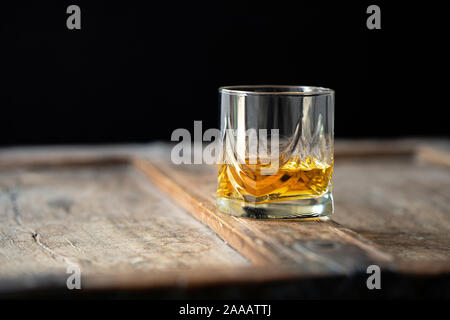 Close up d'un verre de whisky sur une vieille table en bois miteux, fond sombre Banque D'Images