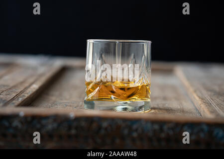 D'un angle faible avec verre de whisky Scotch brillant doré sur une vieille table en bois miteux Banque D'Images
