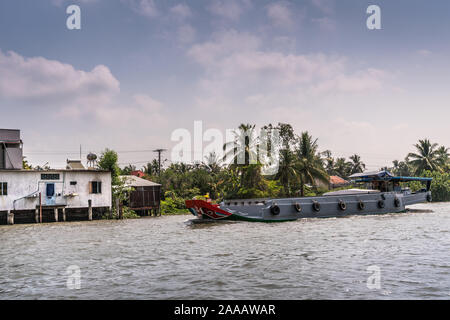 À Cai Be, Delta du Mekong, Vietnam - Mars 13, 2019 : le long du canal 28 Kinh. Barge motorisé gris moderne de la voile sur l'eau brune sous cloudscape bleu. H Blanc Banque D'Images