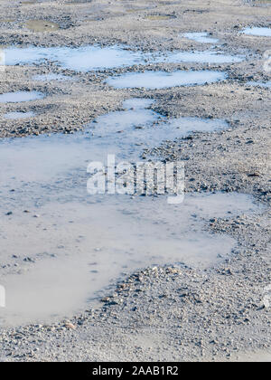 Soleil sur le parking en plein cœur de la mer avec des flaques d'eau stagnante dans les cavités / creux de la poule. Le ciel bleu se reflète dans les flaques, les reflets de l'eau. Banque D'Images