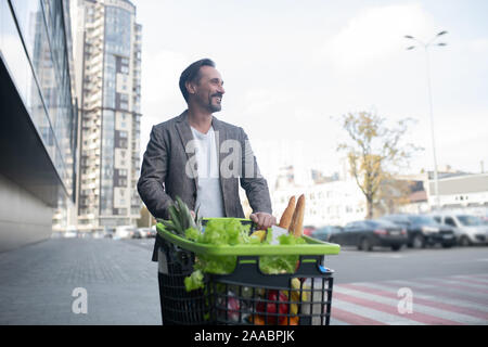 Homme barbu souriant tout en allant à sa voiture après l'épicerie Banque D'Images