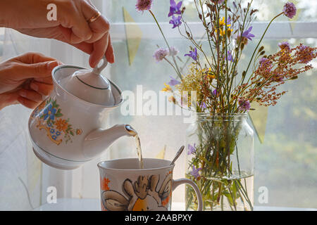 Le thé du matin est versé dans une tasse et un bouquet de fleurs sauvages contre la fenêtre Banque D'Images