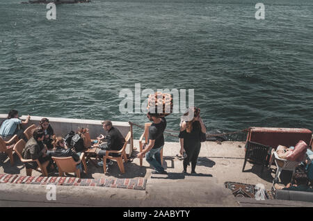 ISTANBUL, TURQUIE : le vendeur de simit - bagels turcs et les visiteurs du café sur le front de mer de Uskudar avec vue sur la tour de la jeune fille le 12 mai 2018 Banque D'Images