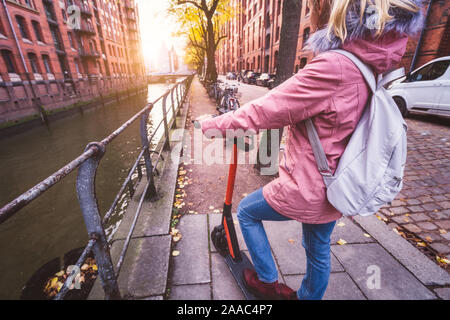 Vue arrière de la femme adultes touriste avec sac à dos découvrir Hambourg ville sur l'e-scooter. Historique Le plus célèbre quartier des entrepôts de Speicherstadt, Allemagne, Eur Banque D'Images